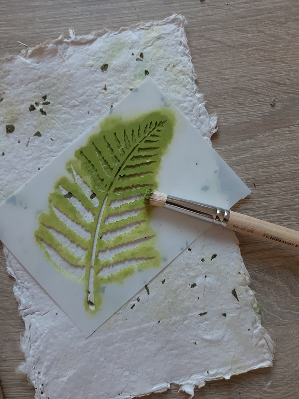 Ein Farnblatt wird mittels einer Schablone auf ein Naturpapier aufgetragen